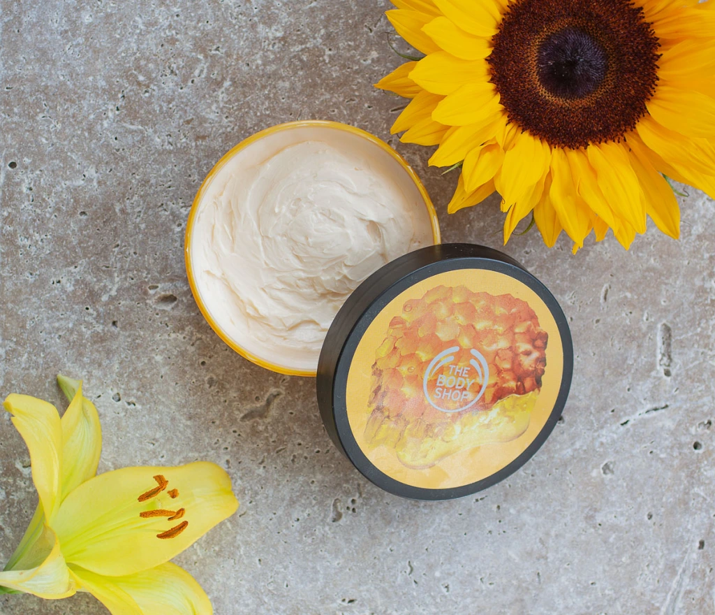 body shop body butter flatlay with sunflower and lilly